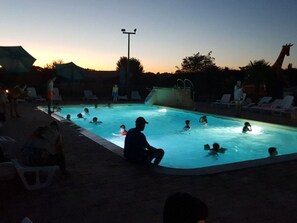 Una piscina rodeada de sillas de descanso y sombrillas, con gente nadando y relajándose.
