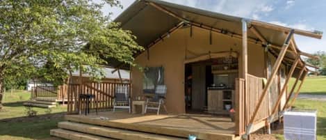 A wooden deck with a covered seating area, a small outdoor kitchen, and a view of a grassy area.