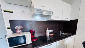 A compact kitchen with white cabinets, a microwave, a red coffee maker, and a sink. - Bright studio at Les 2 Alpes, south balcony, parking (Les Deux Alpes)