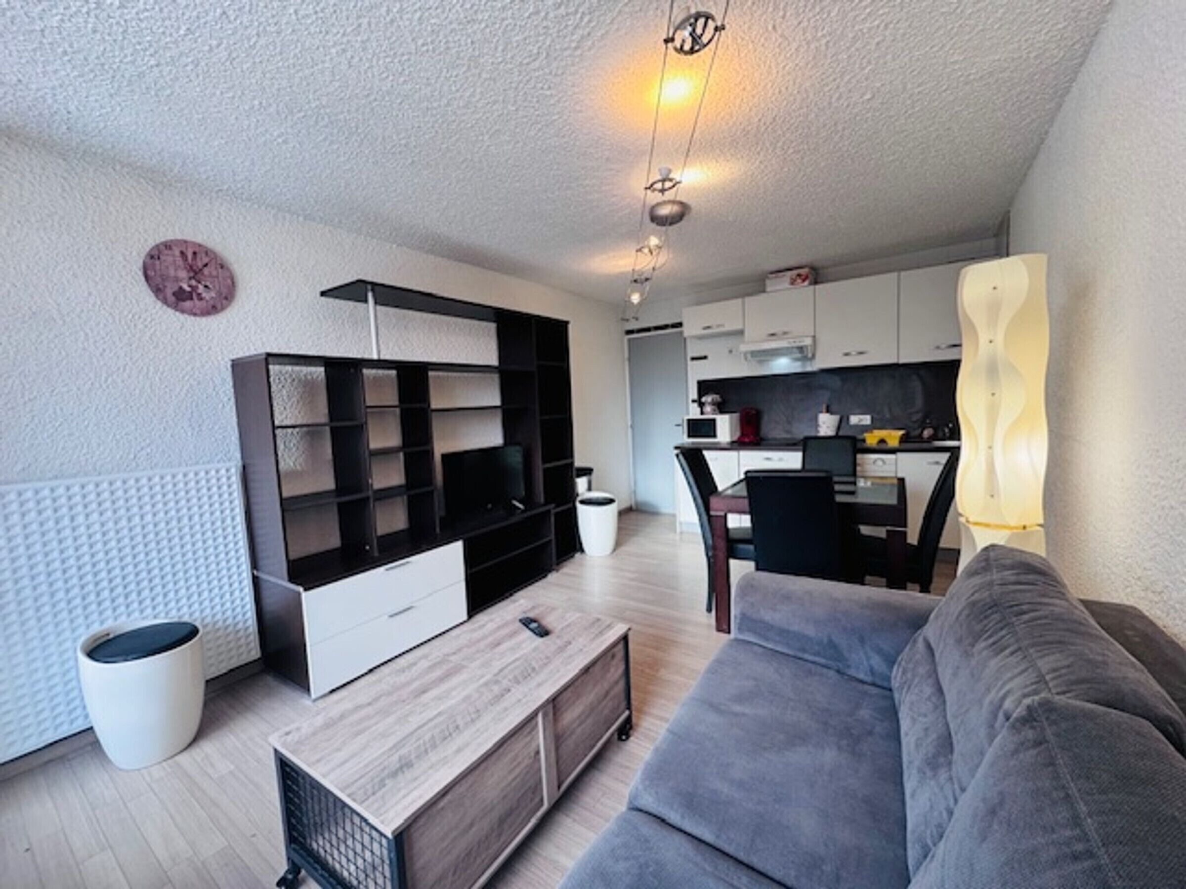 A modern living room with a sofa, a TV, and a kitchen in the background.