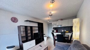 A modern living room with a sofa, a TV, and a kitchen in the background. - Bright studio at Les 2 Alpes, south balcony, parking (Les Deux Alpes)