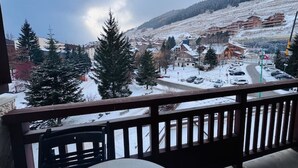 A balcony with a view of a snowy town, including buildings and cars on the road. - Bright studio at Les 2 Alpes, south balcony, parking (Les Deux Alpes)