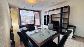 A modern room with a glass-top table, black chairs, a large bookshelf, and a view of the city through a large window. - Bright studio at Les 2 Alpes, south balcony, parking (Les Deux Alpes)