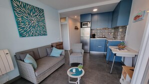 A compact living space with a sofa, a small round table, a kitchen area with blue cabinets, and a decorative wall piece. - Apartment in L'Escala near the beach, 2 bedrooms (L'Escala)