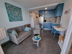 A compact living space with a sofa, a small round table, a kitchen area with blue cabinets, and a decorative wall piece. - Apartment in L'Escala near the beach, 2 bedrooms (L'Escala)