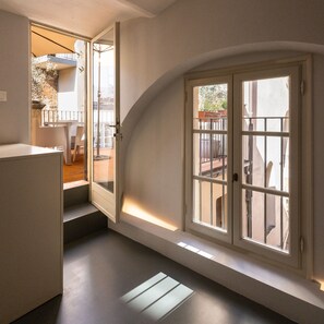A hallway with a door leading to a balcony, a staircase, and a window with a view of the outside.