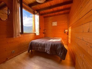 A wooden cabin bedroom with a bed, a window with curtains, a wall-mounted lamp, and a framed picture. - Spacious 130 m² chalet in Crest-Voland with ski shuttle (Crest-Voland)