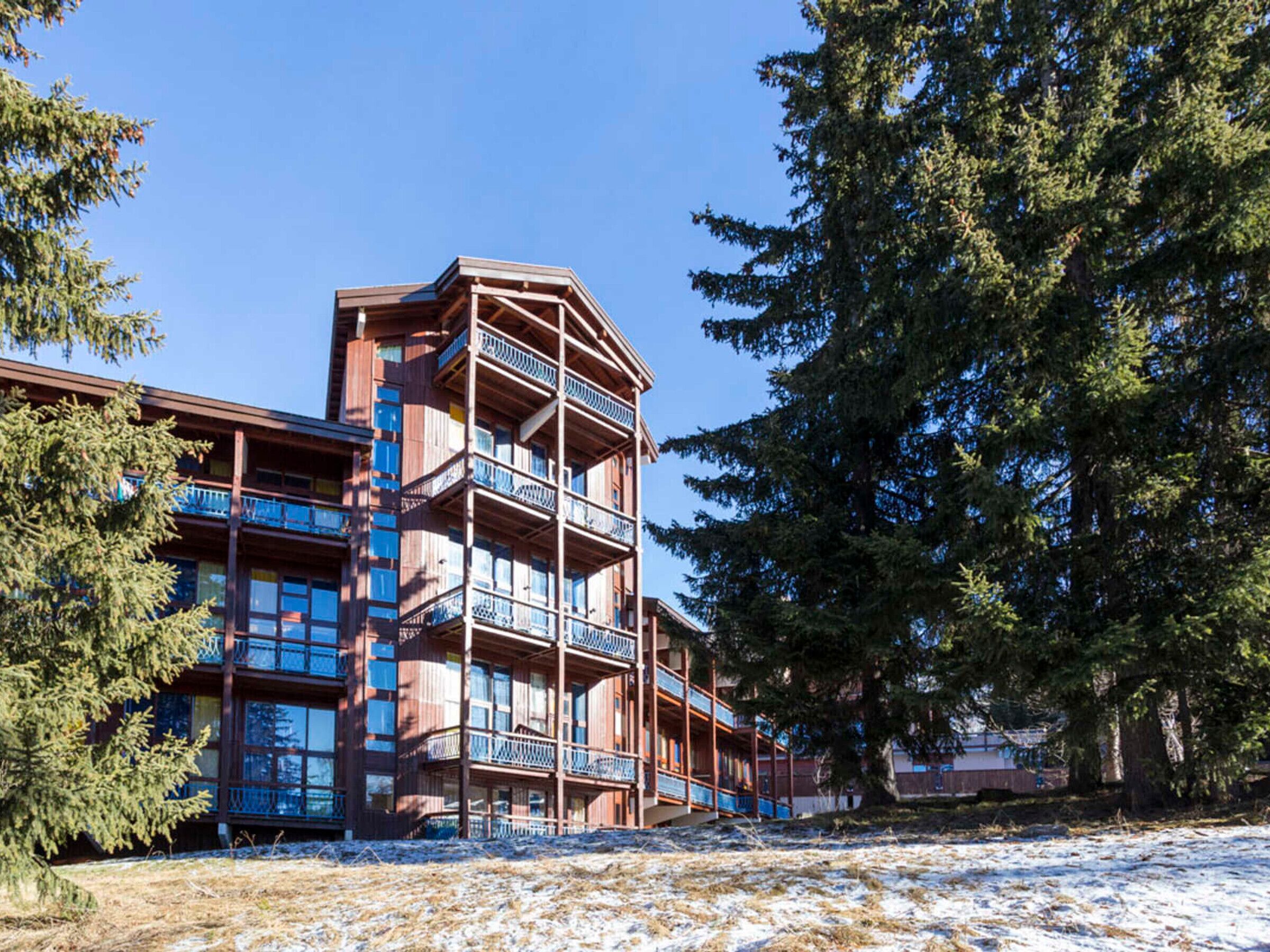 A multi-story building with balconies, surrounded by trees and snow.
