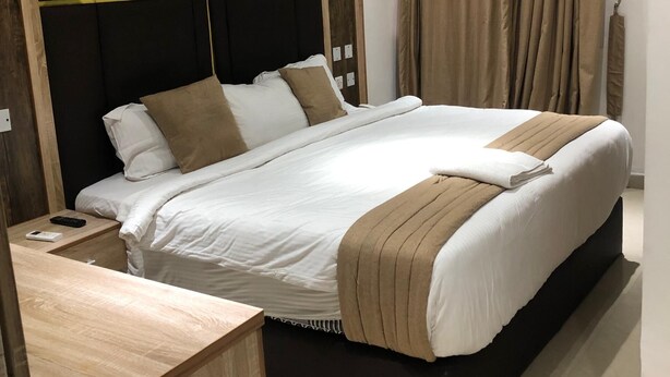 A modern hotel room with a large bed, wooden headboard, and a wooden desk. - Davalon suites & Apartments (Lekki)