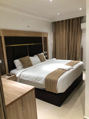 A modern hotel room with a large bed, wooden headboard, and a wooden desk. - Davalon suites & Apartments (Lekki)