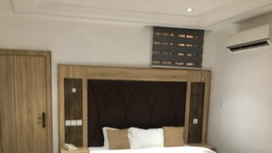 A hotel room with a large bed, a wooden wardrobe, a brown armchair, and a bedside table with a lamp. - Davalon suites & Apartments (Lekki)