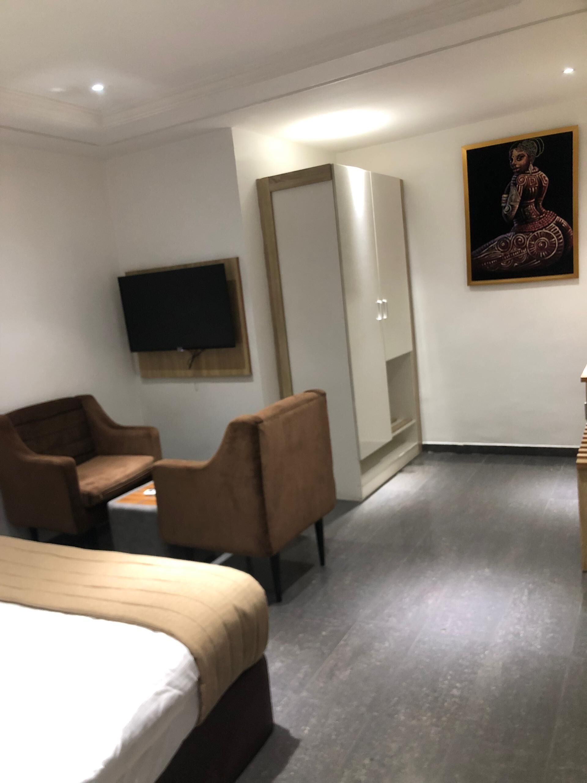 Et hotelværelse med en seng, to lænestole, et fjernsyn, et skab og et billede på væggen.