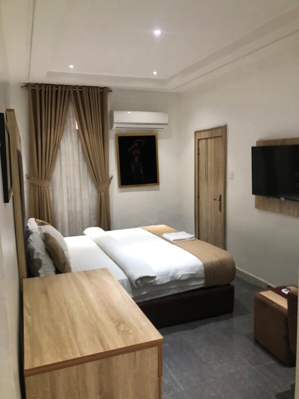 A hotel room with a bed, a TV, an air conditioning unit, and a wooden desk. - Davalon suites & Apartments (Lekki)