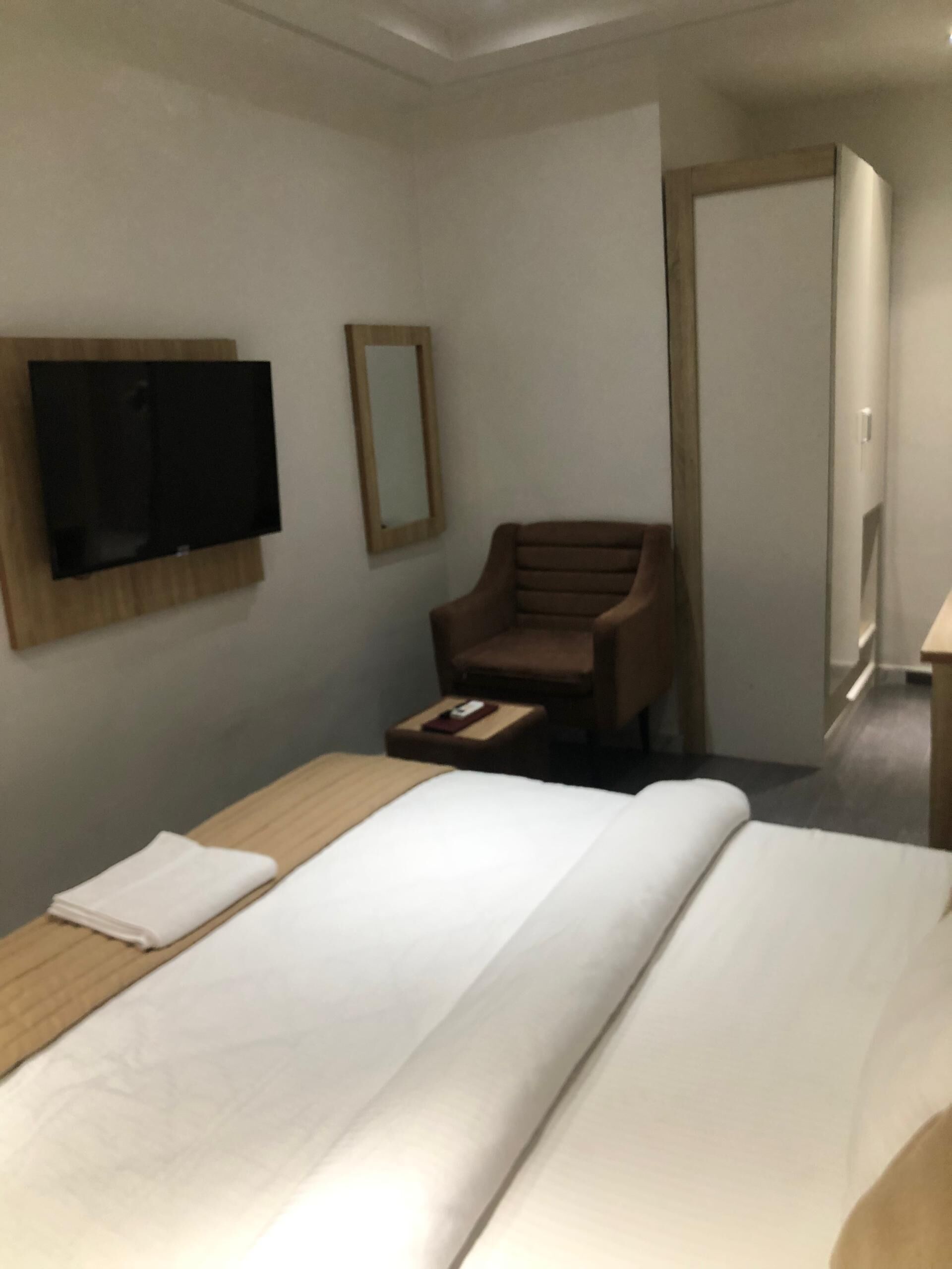 Een hotelkamer met een bed, een aan de muur bevestigde televisie, een stoel en een klein tafeltje.