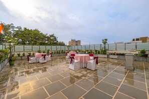 Une terrasse extérieure avec des tables et des chaises, des plantes en pot et un drapeau.