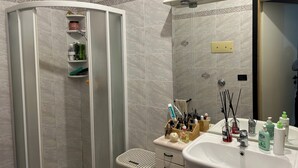 Ein Badezimmer mit Duschkabine, Waschbecken und Pflegeprodukten sowie einem Spiegel.