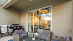 Ein Patio mit Korbmöbeln, einem Grill und einer Glastür zu einem Innenbereich.