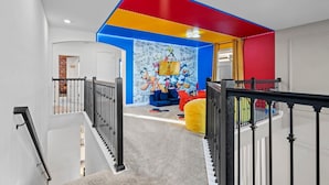 Ein mehrstöckiges Wohnzimmer mit Treppe, einer farbenfrohen Wandmalerei und einem Spielbereich mit Spielzeug.