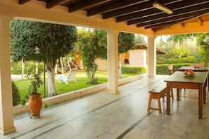 Une terrasse extérieure avec une table et des chaises, entourée d’un jardin et offrant une vue sur un bâtiment.