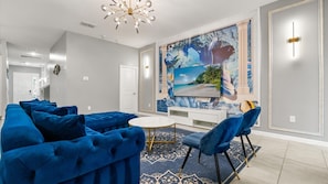 Ein modernes Wohnzimmer mit einem großen Fernseher, blauen Sofas, einem runden Couchtisch und einem gemusterten Teppich.