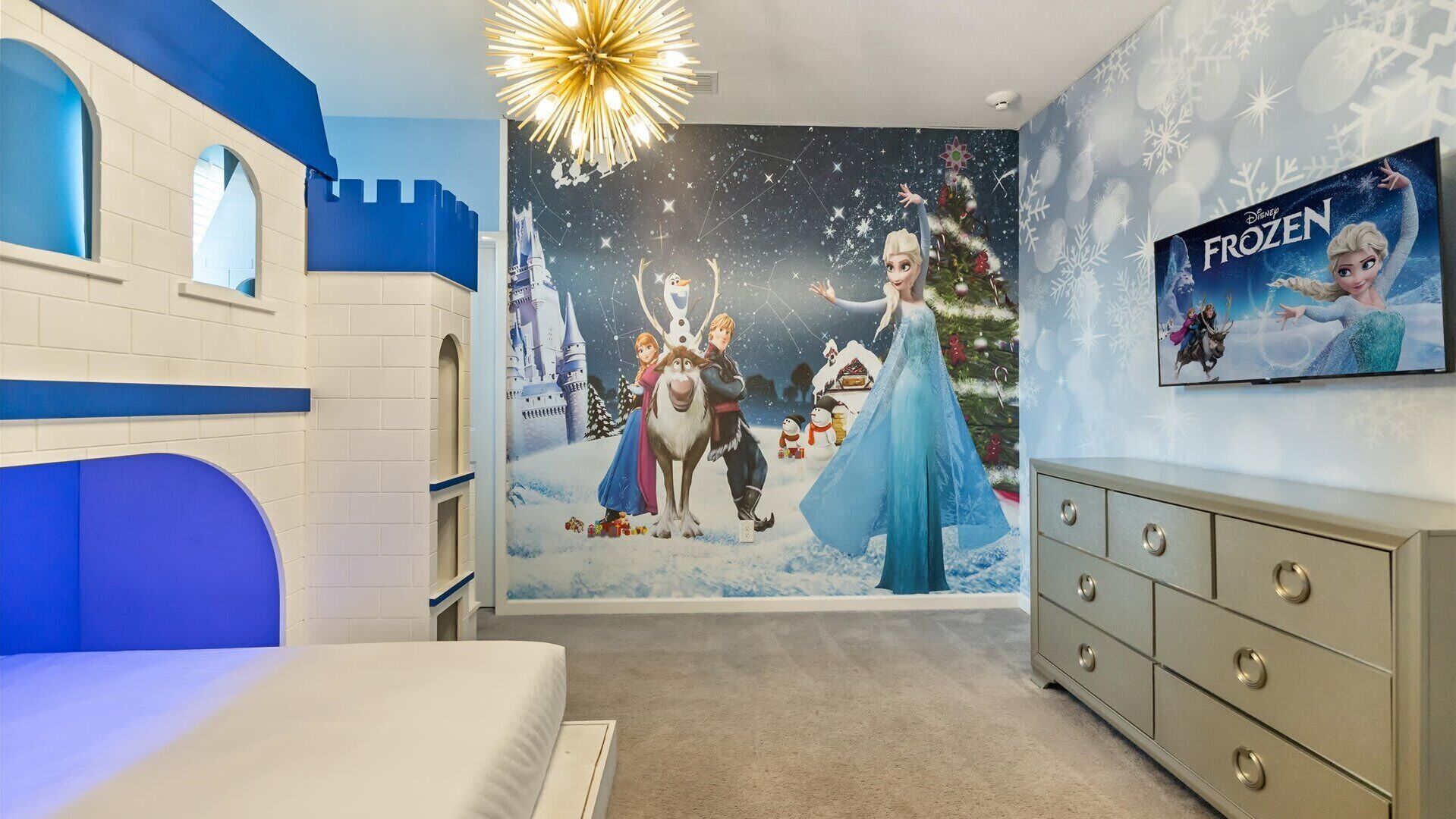 Une chambre avec un décor mural sur le thème d’un château, un lit, une commode et un téléviseur diffusant le film « La Reine des neiges ».