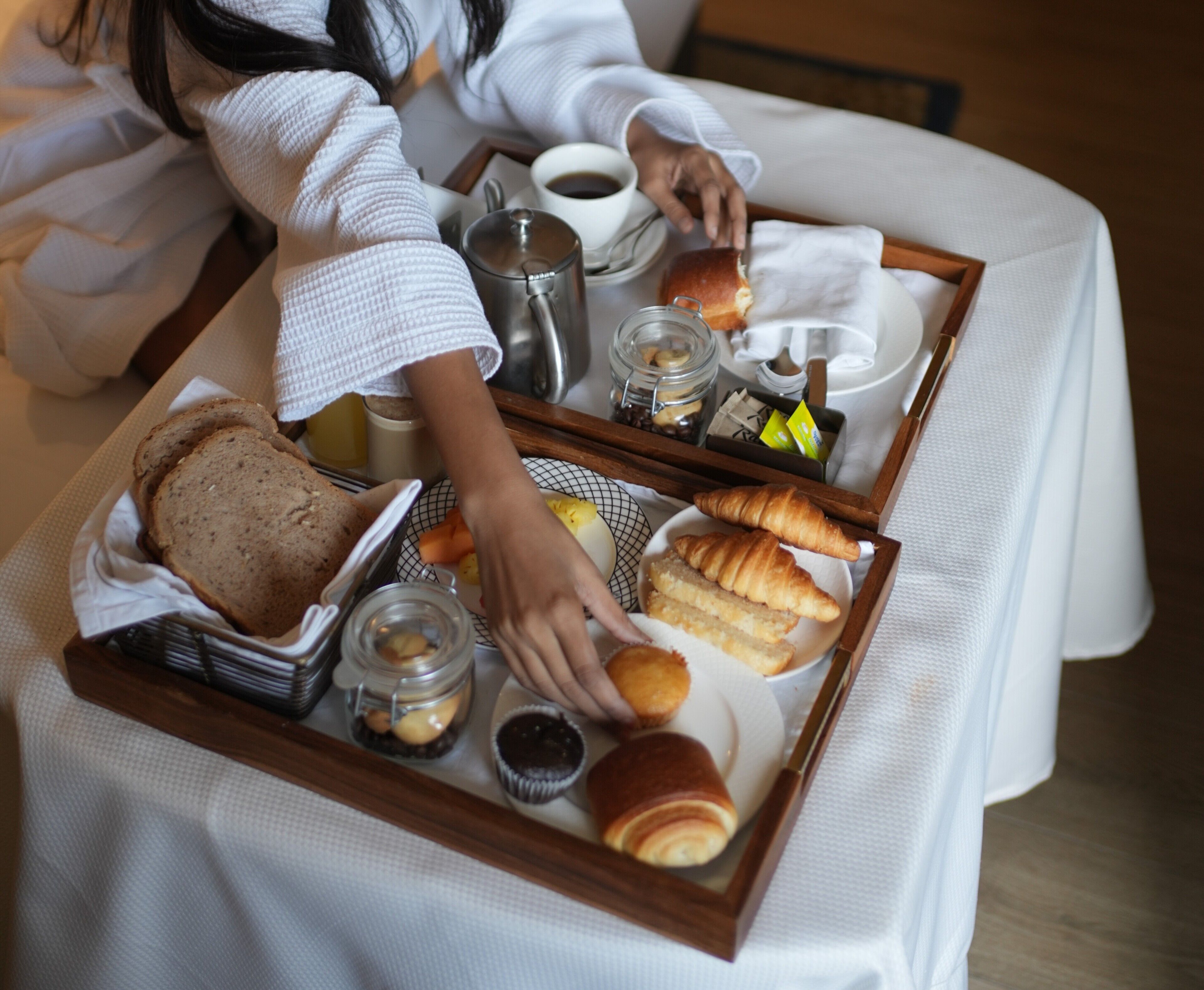 A breakfast tray with bread, pastries, and a coffee pot on a table.
