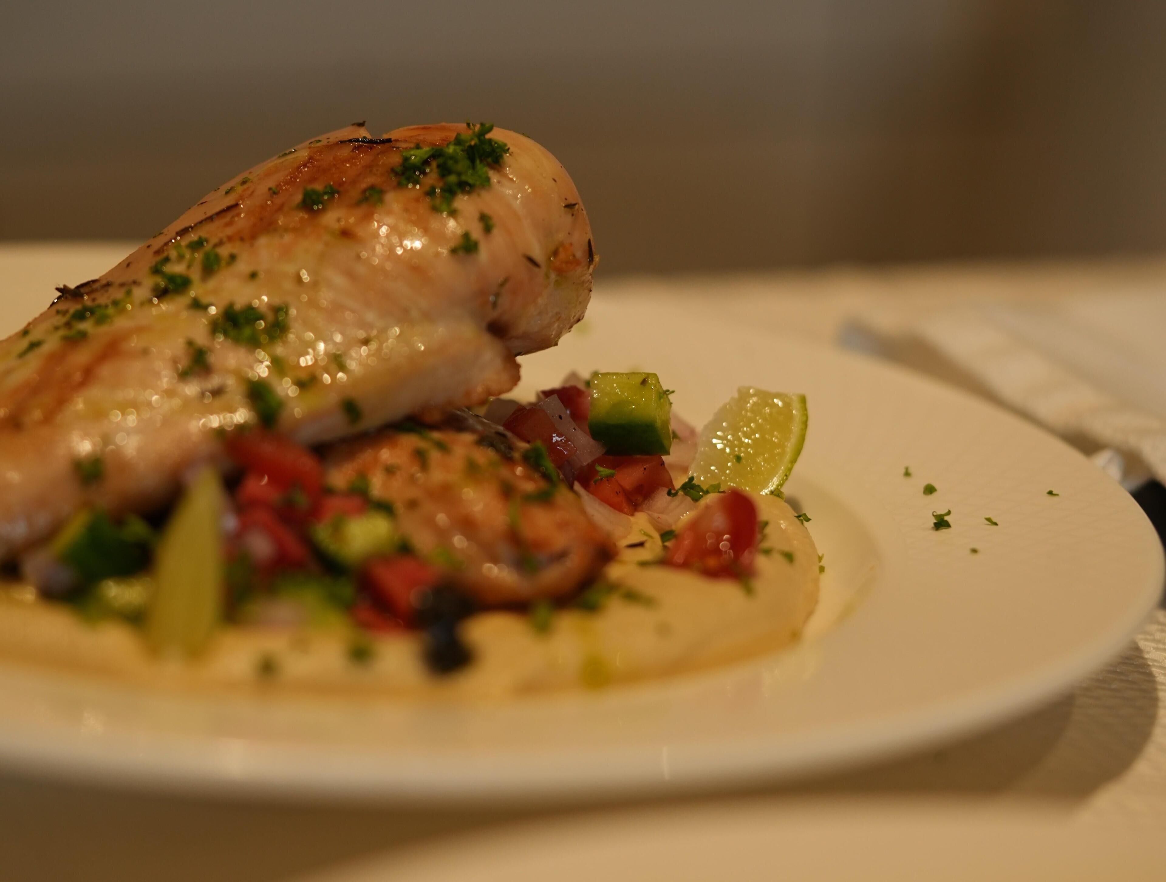 En tallrik med en bit grillad kyckling, tärnade grönsaker och en skiva lime.