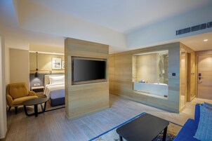 A modern hotel room with a bed, sofa, TV, and bathroom.