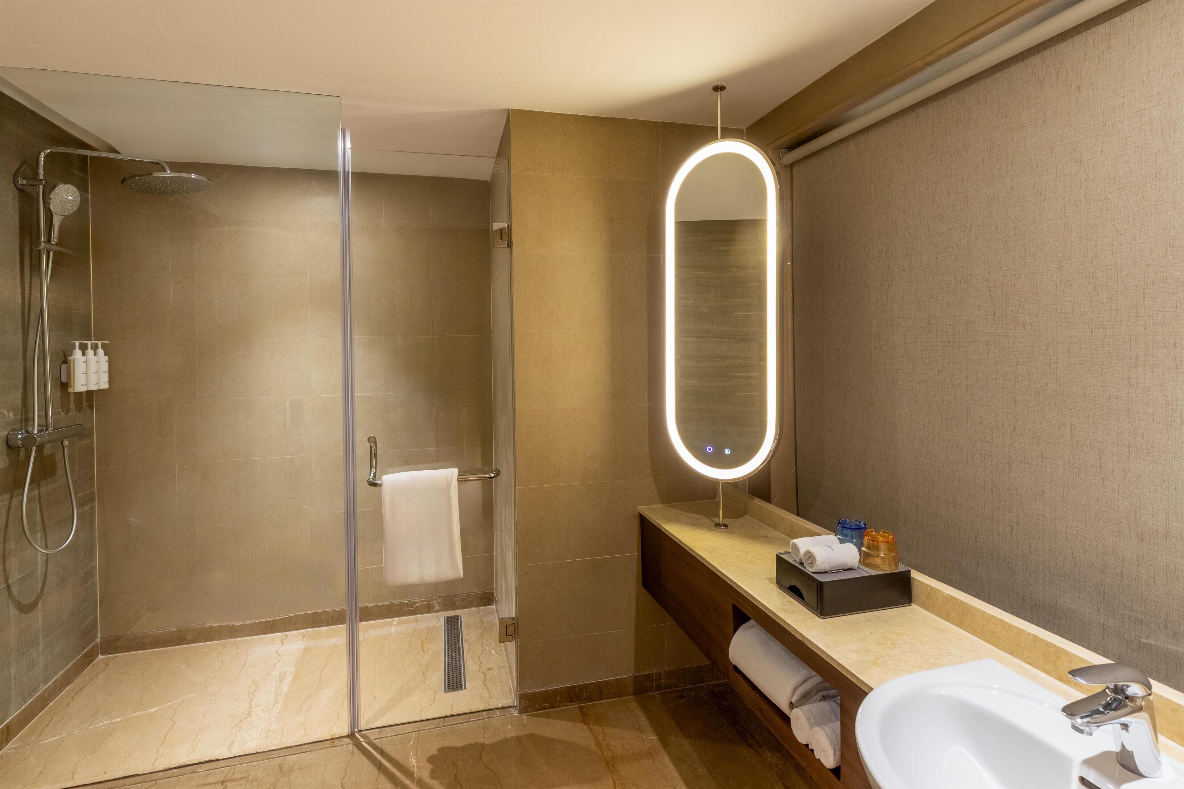 Un baño moderno con cabina de ducha de vidrio, tocador con espejo y lavamanos.