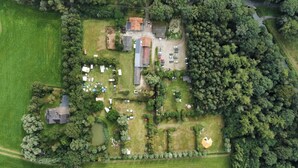 Vue aérienne d’une propriété comprenant plusieurs bâtiments, un espace de stationnement et des espaces verts environnants.