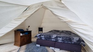Une tente équipée d’un lit, d’une commode et d’un tapis.
