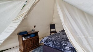 Une tente avec un lit, une petite armoire en bois et une chaise.
