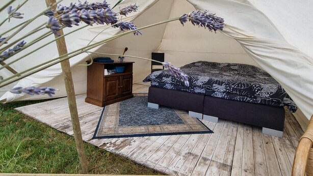 Une tente équipée d’un lit, d’une table en bois et d’une petite armoire.