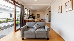 Uma sala de estar moderna com um sofá cinzento, piso de madeira, área de refeições e varanda com plantas.