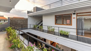 Um edifício residencial moderno, com vários níveis, varandas, escadarias e plantas em vasos.
