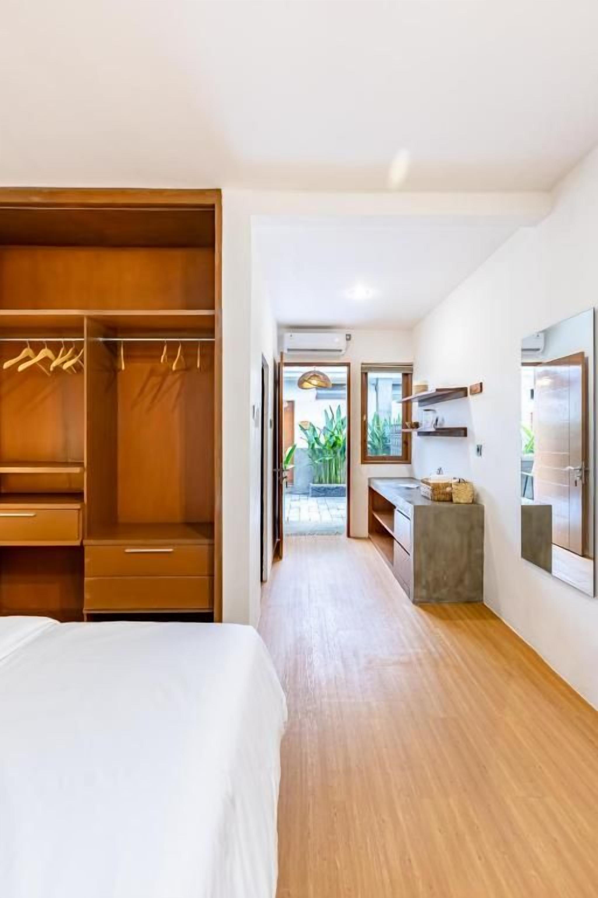 A hotel room with a wooden floor, a bed, a wardrobe, a desk, and a view of the outdoors.