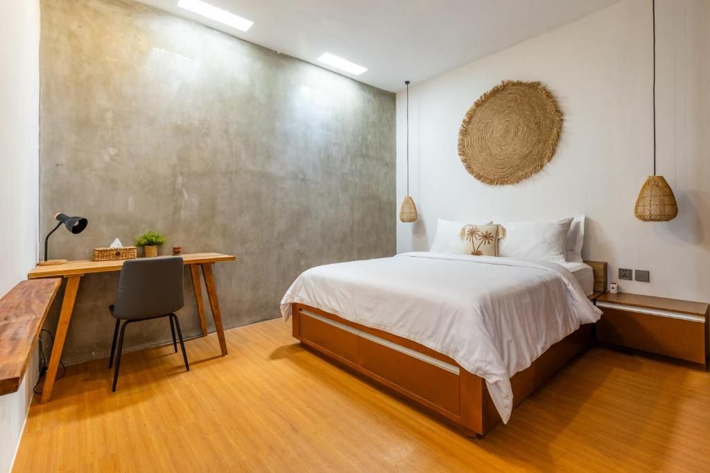 A bedroom with a bed, bedside tables, a desk, a chair, and a hanging light fixture.