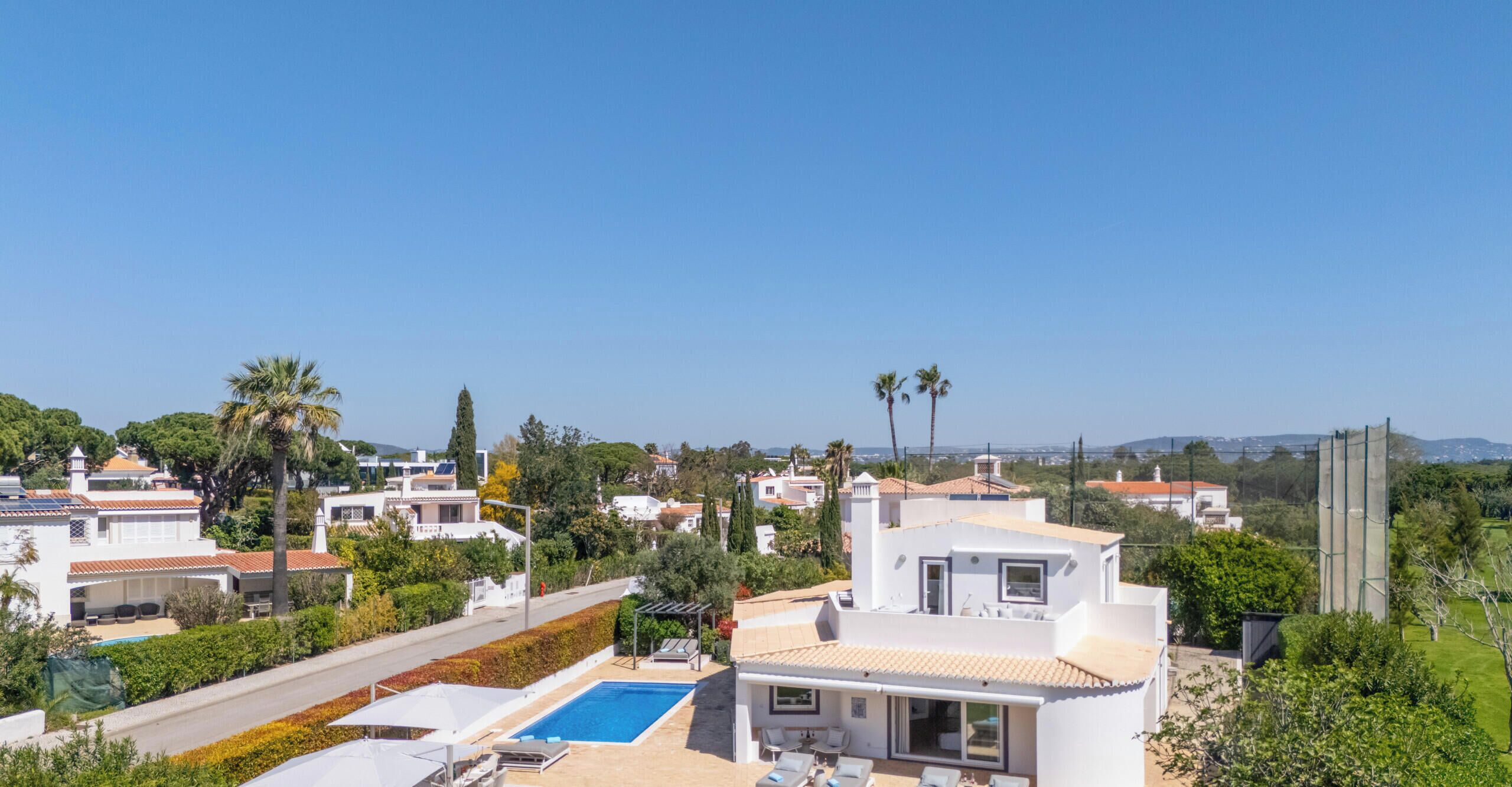 A residential area with modern houses, a swimming pool, and a clear blue sky.