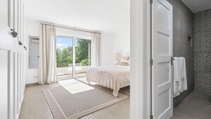 Ein modernes Schlafzimmer mit einem großen Bett, einer Schiebetür zum Balkon und einem Badezimmer mit gemusterten Fliesen.
