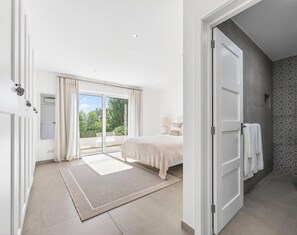 Ein modernes Schlafzimmer mit einem großen Bett, einer Schiebetür zum Balkon und einem Badezimmer mit gemusterten Fliesen.