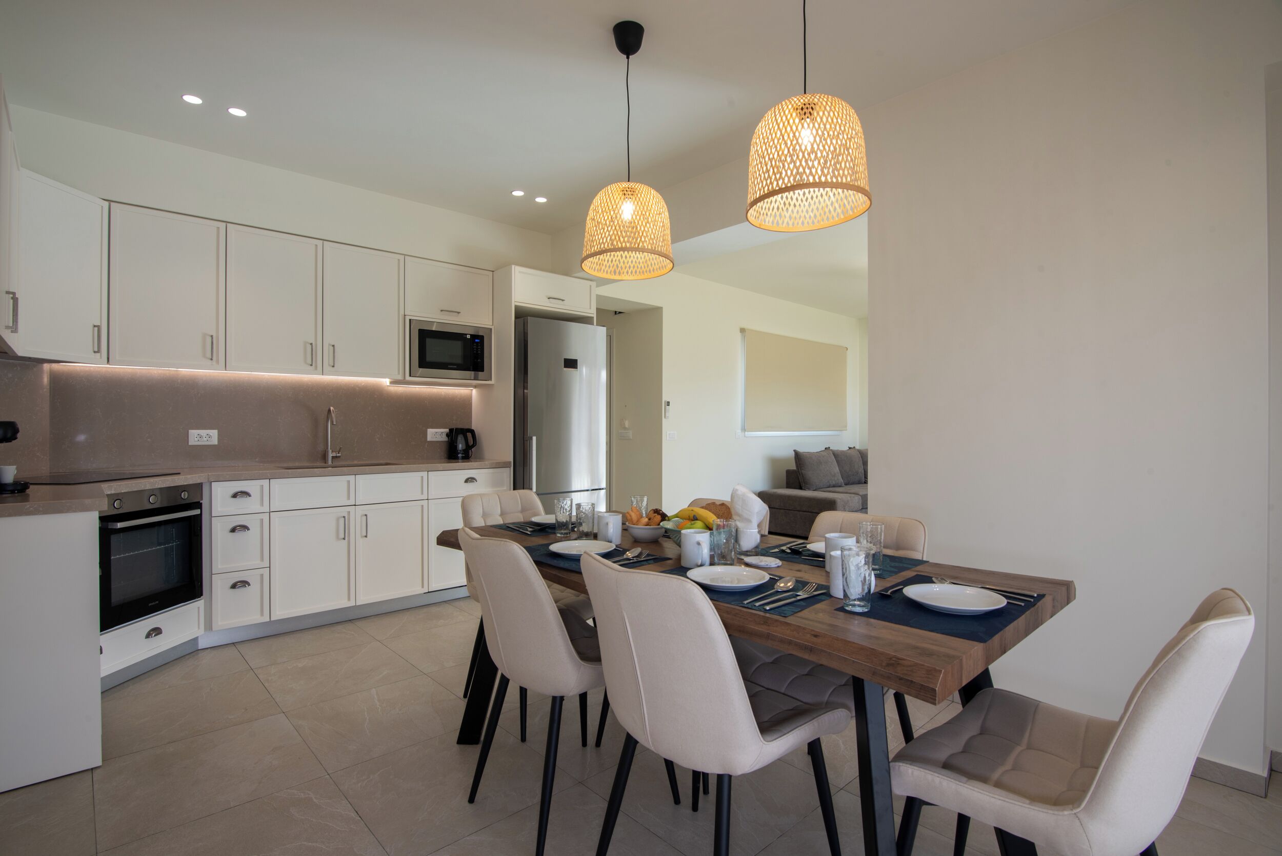 A modern kitchen with white cabinets, a wooden dining table, and two hanging pendant lights.