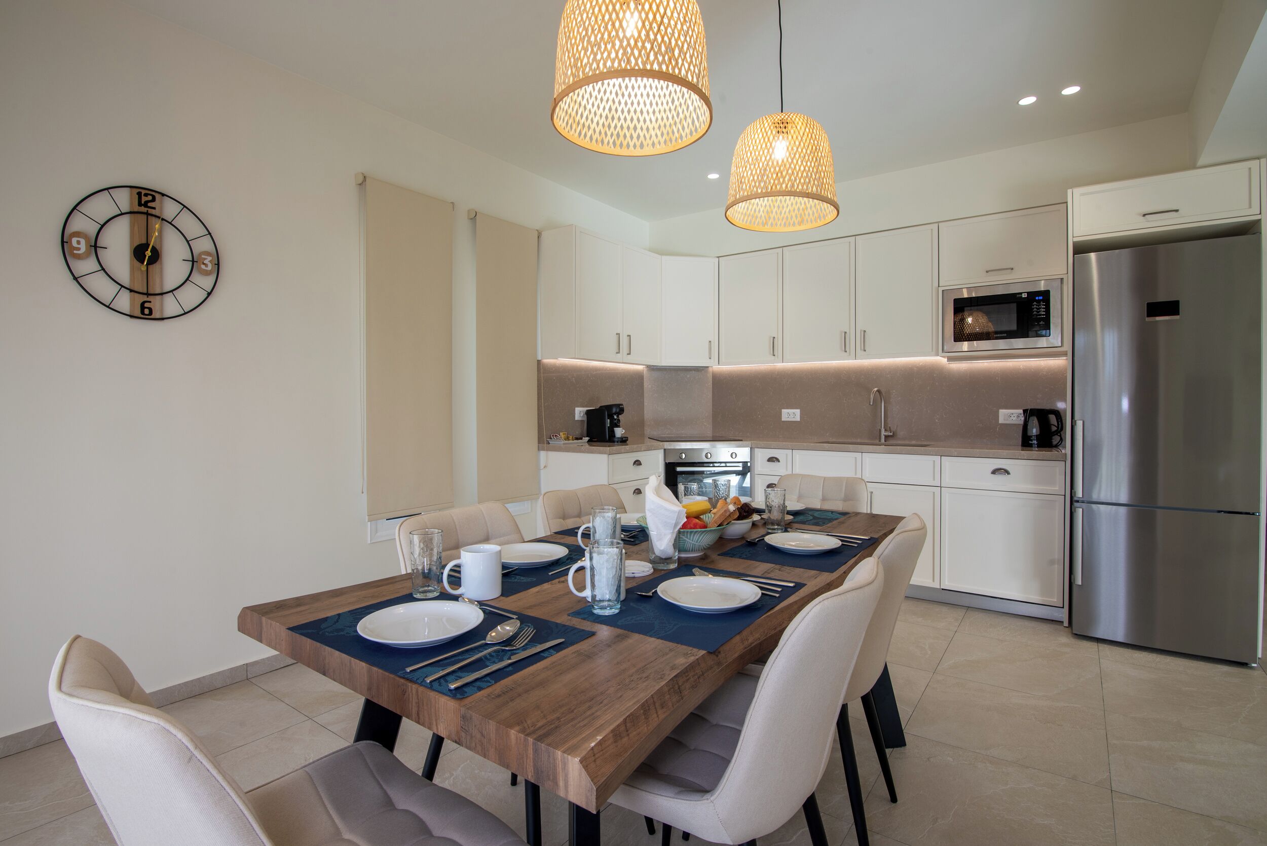 A modern kitchen with white cabinets, a stainless steel refrigerator, a microwave, and a dining area with a wooden table set for four.