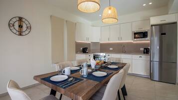 A modern kitchen with white cabinets, a stainless steel refrigerator, a microwave, and a dining area with a wooden table set for four.