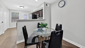 Una cocina moderna con comedor, que incluye una mesa redonda de vidrio, sillas negras y un reloj en la pared.