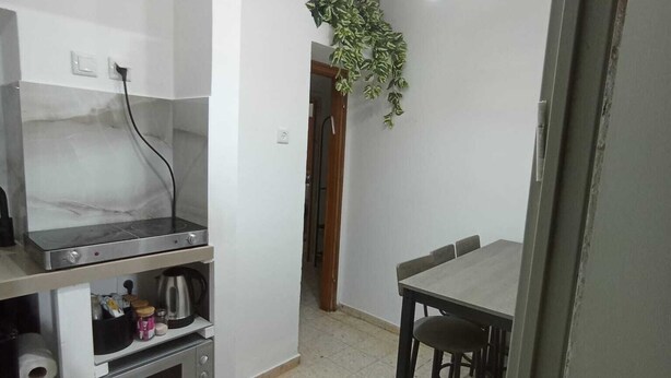 A compact kitchen with a gas stove, a small oven, and a sink. There are hanging pendant lights and a potted plant.