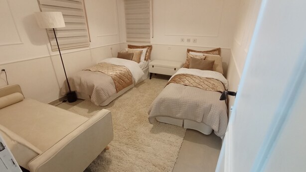 A bedroom with two beds, a bedside table, a lamp, and a window with blinds. - 1-bedroom, AC, Wifi, 10 minutes from Rashbi, 3 minutes from Safed Old City (Safed)