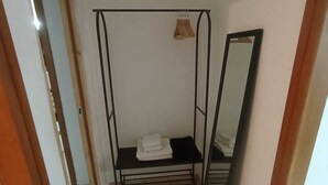 A room with a metal bed frame, a small table with folded towels, a mirror, and a tiled floor.