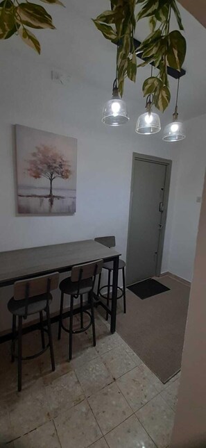 A dining area with a table and chairs, a painting of a tree, and hanging lights. - 1-bedroom, AC, Wifi, 10 minutes from Rashbi, 3 minutes from Safed Old City (Safed)