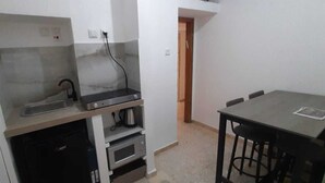 A compact kitchen with a sink, stove, and oven, a dining table with chairs, and a small hallway leading to another room.