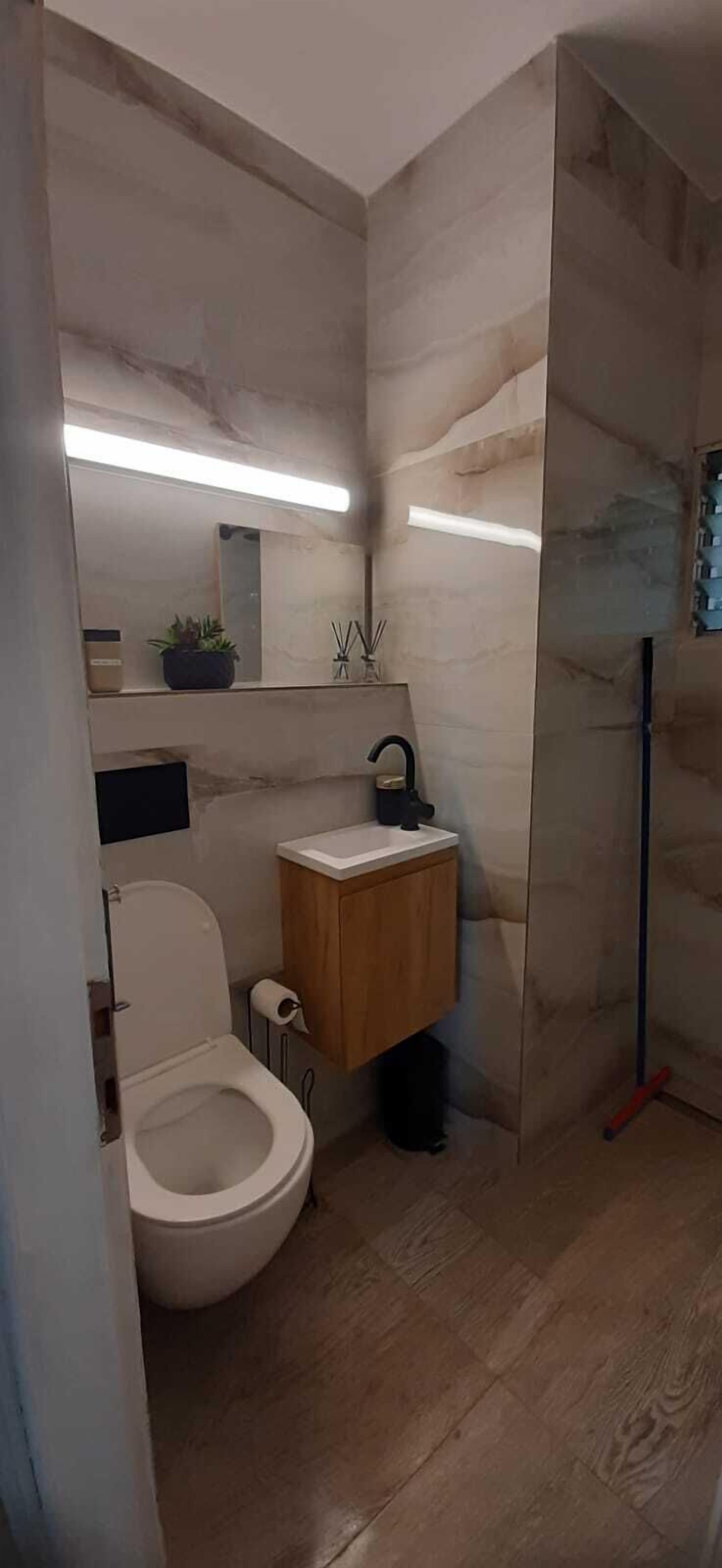 A modern bathroom with a toilet, sink, mirror, and a shower area.